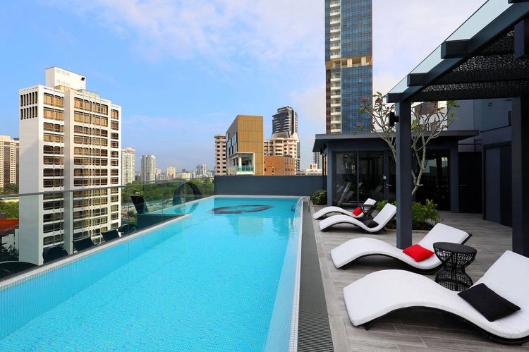 Rooftop infinity pool at Oakwood Studios Singapore with lounge chairs, city skyline, and clear blue sky